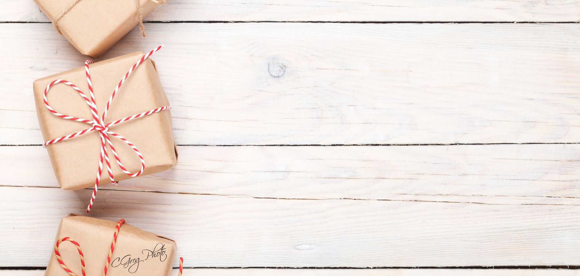 carte cadeau 2 Trois petits paquets en papier kraft, ficelés avec soin. L’une des ficelles est rouge et blanche, elle ressort juste assez. Ils sont posés sur le bord gauche d’une vieille table en bois blanc, bien alignés. À droite, il reste un grand espace vide, comme si on attendait quelque chose.